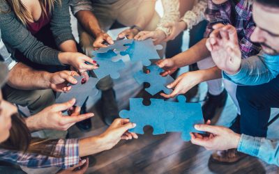 Businesspeople joining puzzle pieces in office, close up.